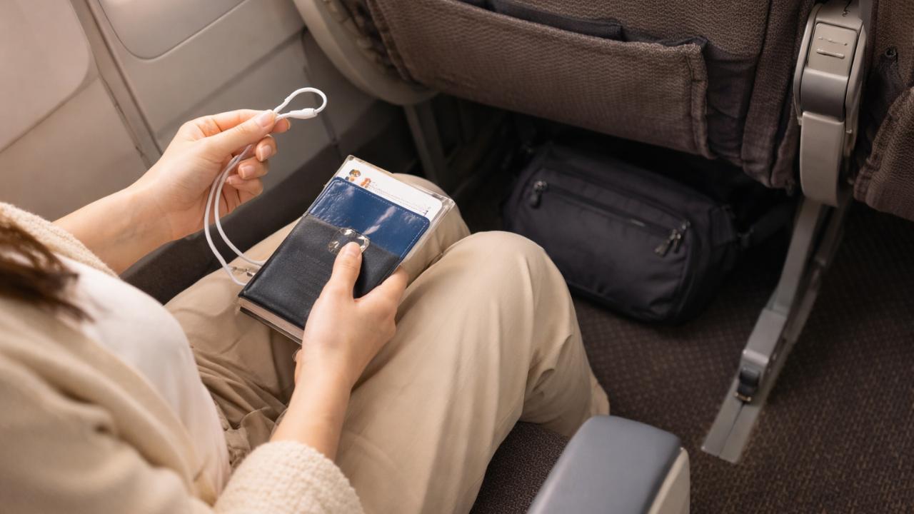 機内の座席、足元に小さな斜めがけバッグ、手元にイヤホンとパスポート控え
