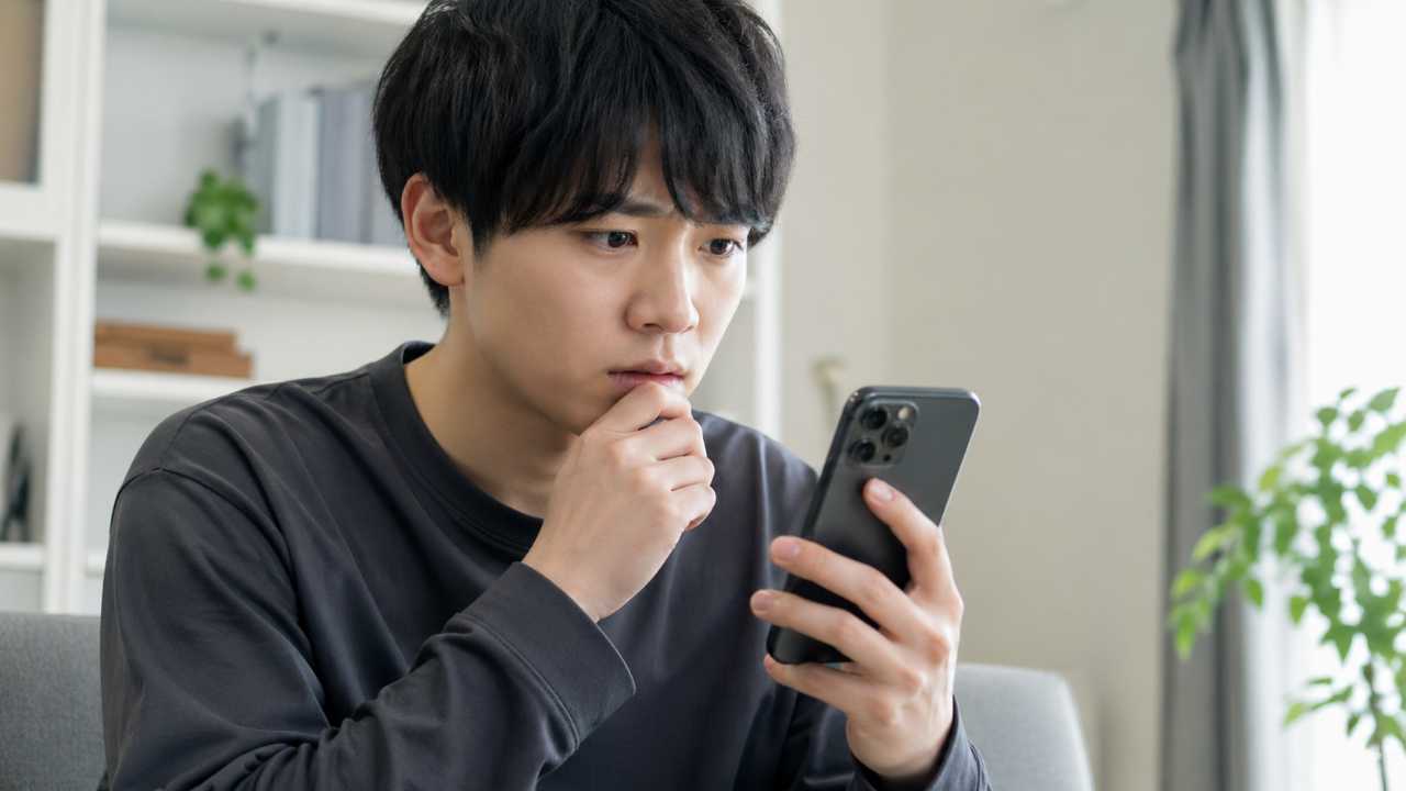 スマートフォンに怪しい求人通知が表示され、手前の若者が不安そうに画面を見つめている